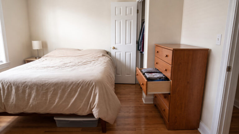 Small bedroom with a bed, closet and a dresser drawer opening into the narrow walking route.