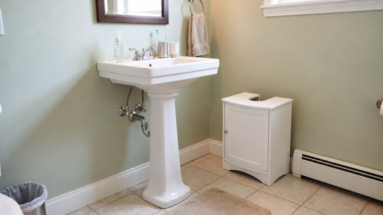 Pedestal sink beside a separate cabinet with a U-shaped opening in a small bathroom.