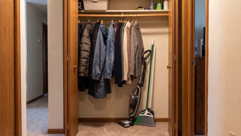 Coats hanging in a hallway closet beside a vacuum and cleaning tools, showing the competition for usable storage space.