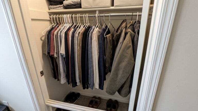 Shallow reach-in closet with hanging clothes projecting toward the opening, showing limited usable depth for additional storage.